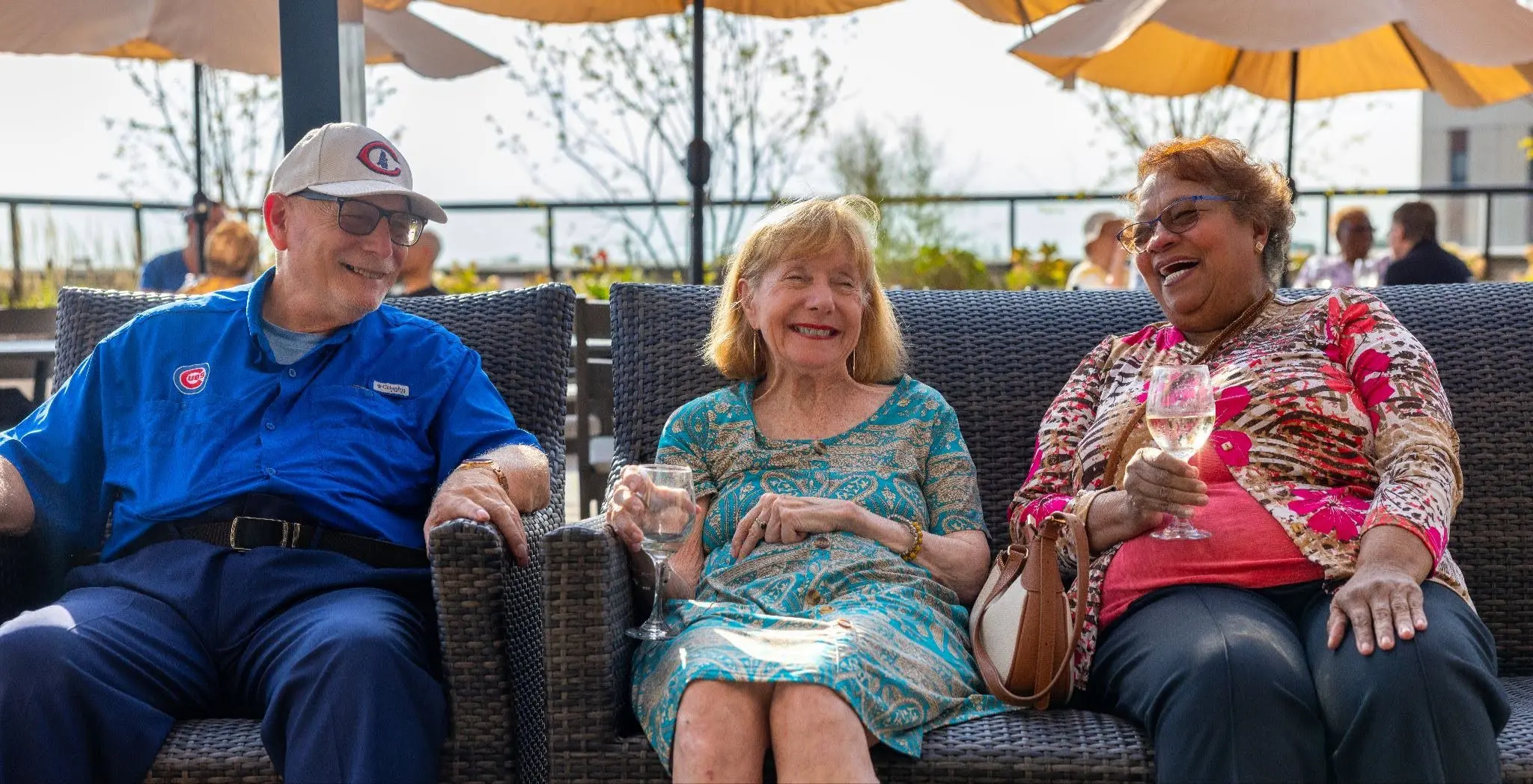 Three seniors enjoying wine and sitting outside on chairs, enjoying upscale senior living at Clarendale Six Corners in Chicago, IL.