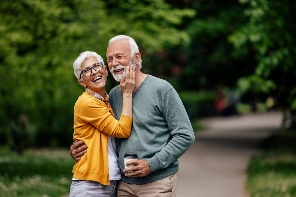 A smiling mature couple hugging outside on a walking path in a park