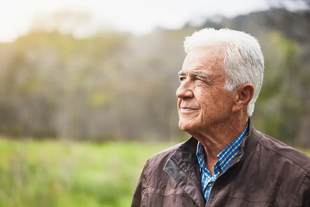 Handsome man in his late 70s looks pensive as he stares out into the distance.