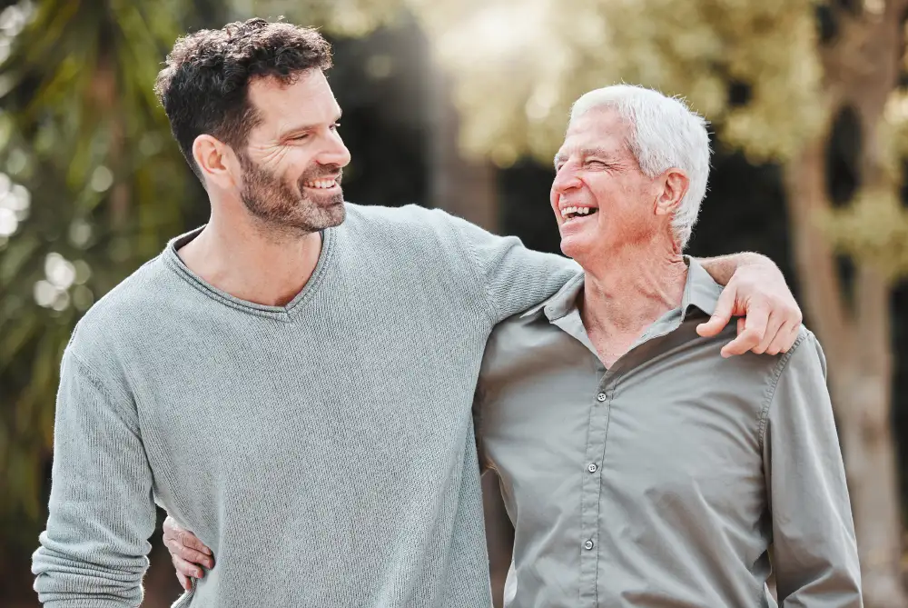 a man with his arm around his senior father as they walk outside at a memory care community
