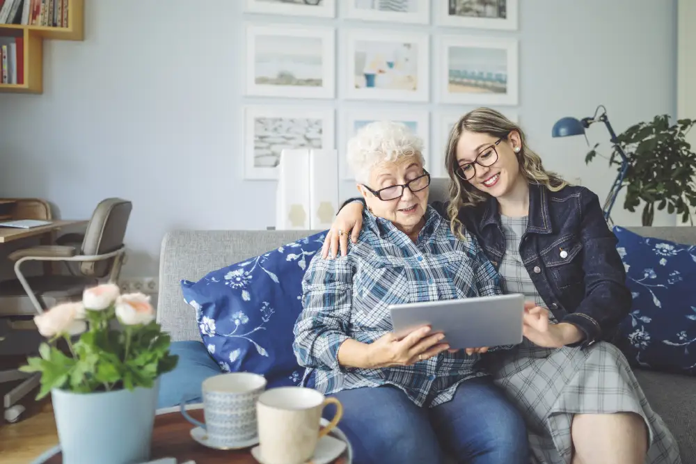 a woman and her senior mother reading on a tablet device at a memory care community