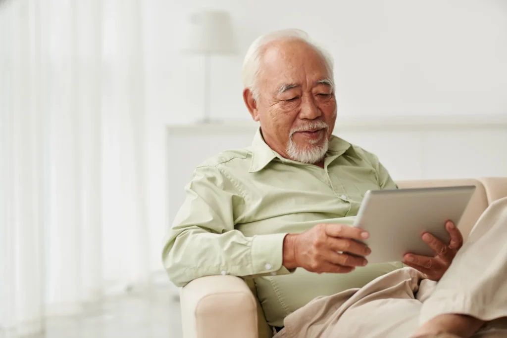 An elderly Asian man reading books on aging well from his home at Clarendale Six Corners in Chicago, Illinois.