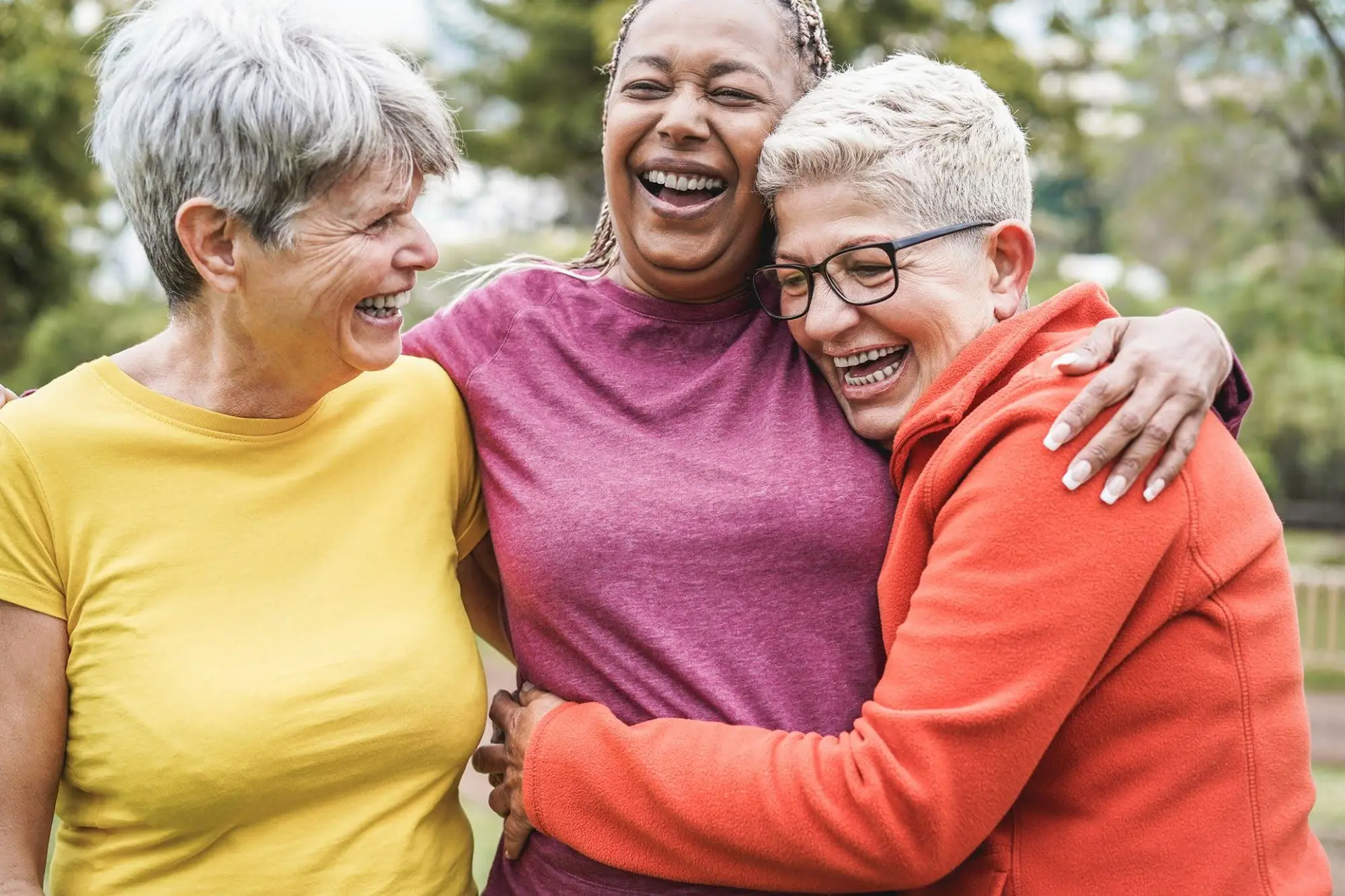 Three senior women smiling & hugging while aging in place at Clarendale Six Corners in Chicago.